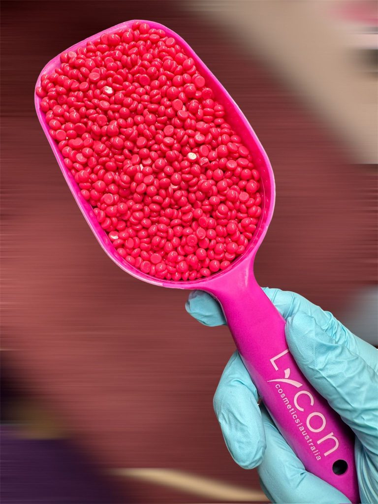 Close-up of Lycon hot wax beads in a pink waxing scoop, held by a beauty therapist wearing blue gloves, used for professional waxing treatments in London.